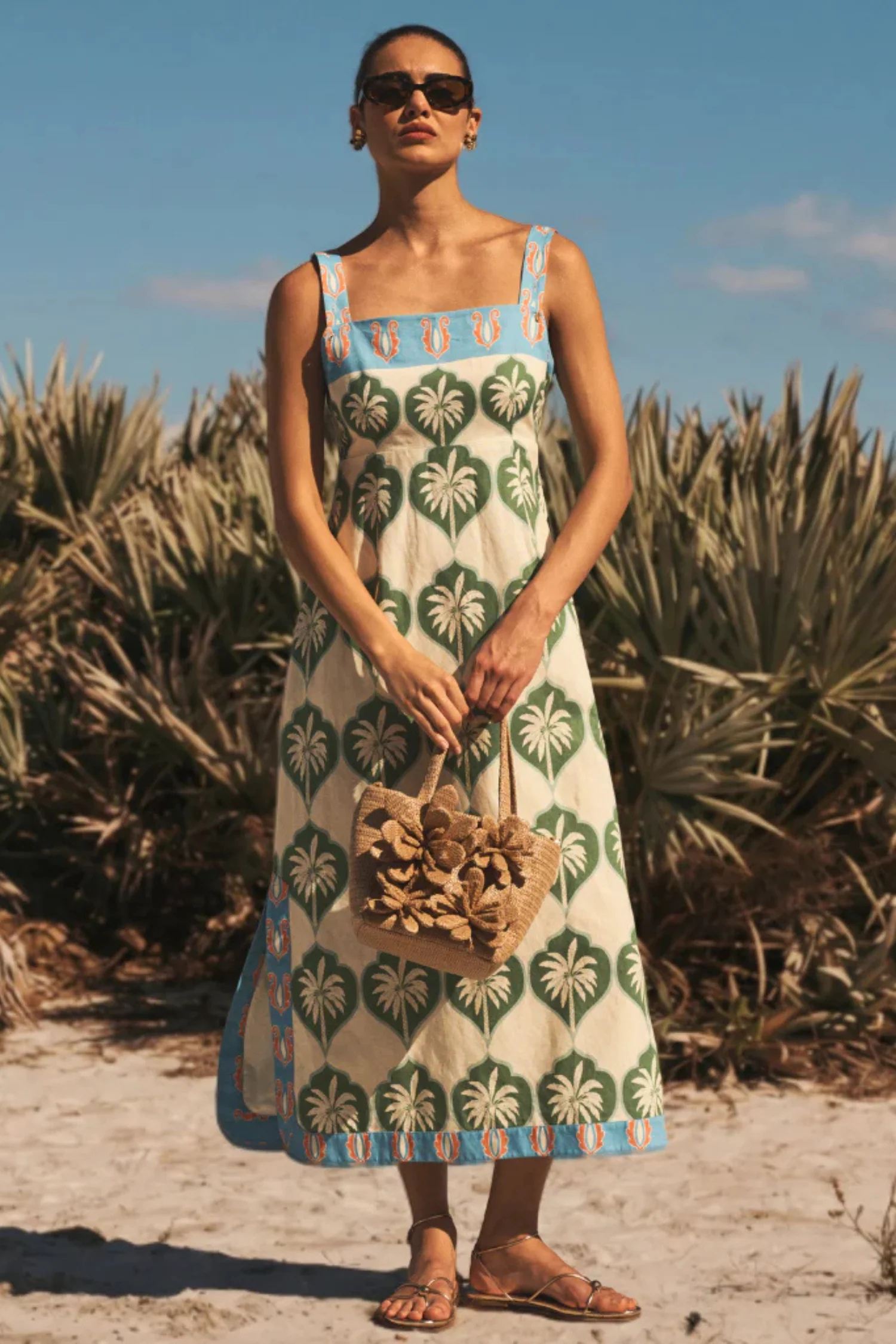 Woman in a patterned dress standing in a desert-like setting with palm trees.
