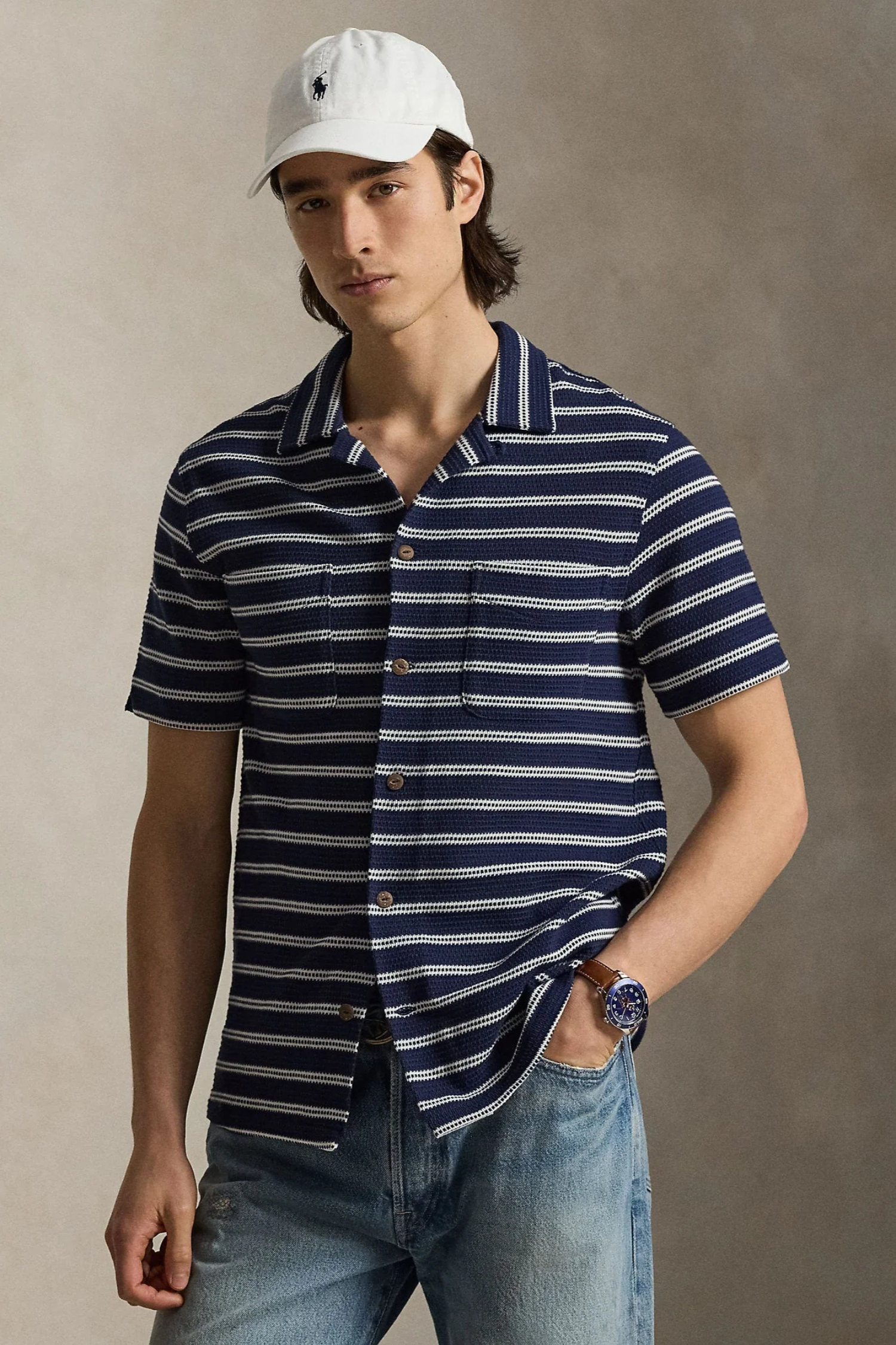 Man wearing a navy and white striped shirt with a white cap against a neutral background