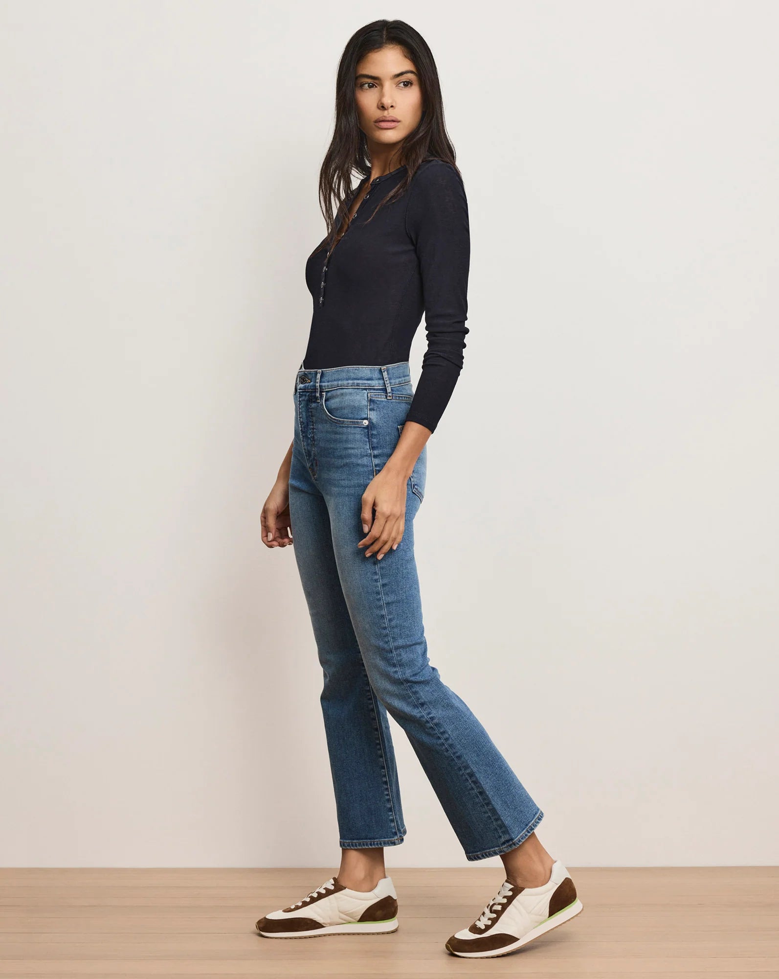 A woman wearing a black top with blue jeans and white and brown shoes