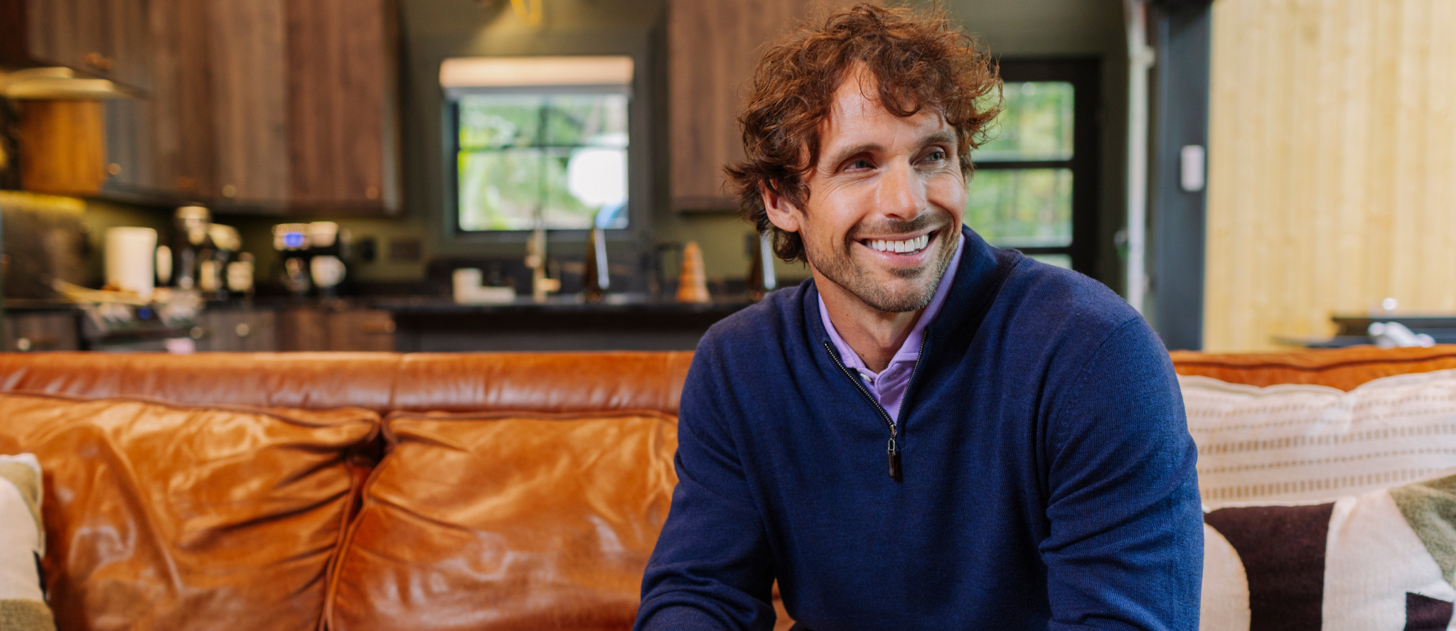 Man sitting on a couch in a living room with a kitchen in the background